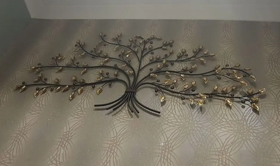 A metal tree with gold leaves, on a papered wall